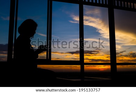 Girl playing smart phone by window at sunset with twilight sky