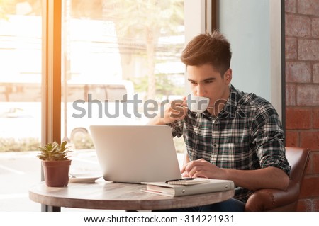 Businessman using laptop with tablet and pen on wooden table in coffee shop with a cup of coffee