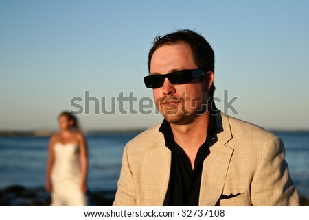 A portrait of a smiling groom with the bride in the background