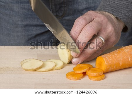 Mans hands chopping vegetables on wooden chopping board