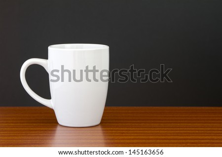 White mug on dark wooden table with black wall