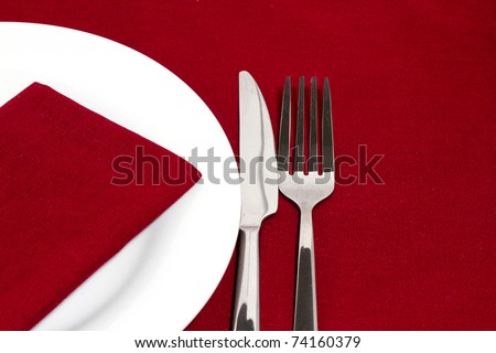 Knife and fork with white plate on red tablecloth