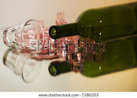 Bottle with ice cubes and some spilled red wine on a reflecting surface.