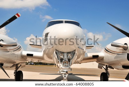 Twin engine plane on the tarmac for scheduled maintenance. The nose end and lights are the focal point of this speedy corporate plane. The props, engines and landing gear are partially visible.