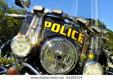 The view of the front end of a Police motorcycle parked at the station. Lights, blinkers and emergency flashers are all seen in this fully customized, two wheeled law enforcement bike.