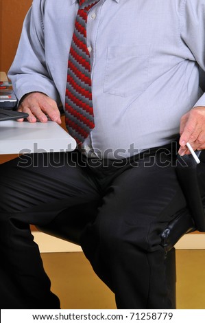 Middle age business man sitting at his desk preparing to leave for a cigarette break. His heavy stomach suggests he is sedentary and needs to exercise and stop smoking.