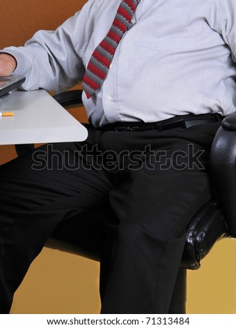 Middle aged business man sitting at his desk working. Man\'s poor posture and physical appearance along with seeing the butt of a cigarette may show bad lifestyle and could lead to physical problems.