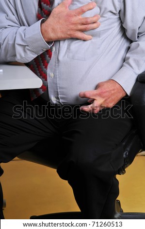 Middle aged,overweight man having a heart attack at his desk. Hand grasping his heart and pain radiating down his arm cramping his hand.