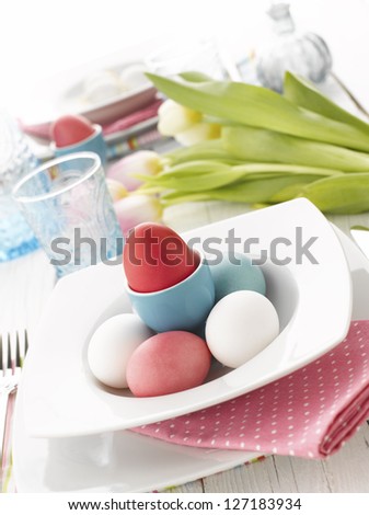 An elegant holiday table setting with colorful easter eggs and flowers. White wooden table background.