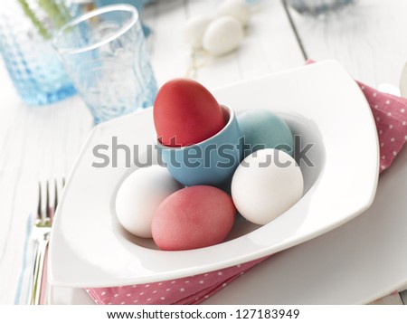 An elegant holiday table setting with colorful easter eggs. White wooden table background.