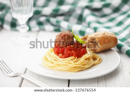 Plate of spaghetti with meatballs in tomato marinara sauce and ingredients on white wooden table