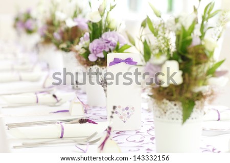 A fresh bouquet of flowers lies on a white wedding reception table setting. Shallow focus.