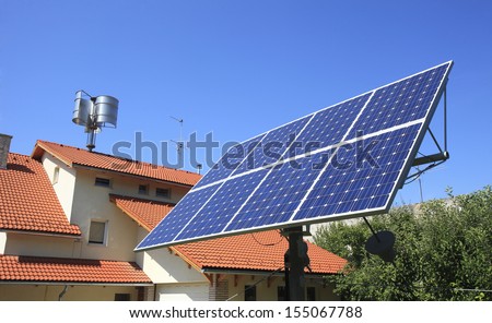 Alternative energy. Family house with solar power panels and wind turbine generator against a deep blue sky