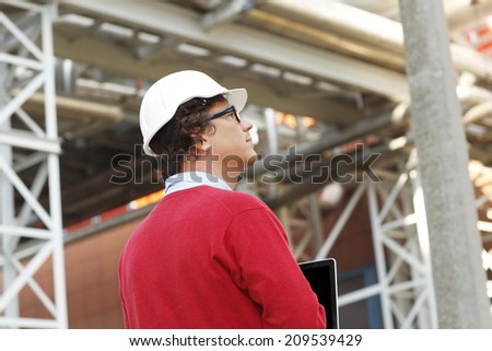 Close-up of construction worker wearing hardhat and holding laptop at construction site.