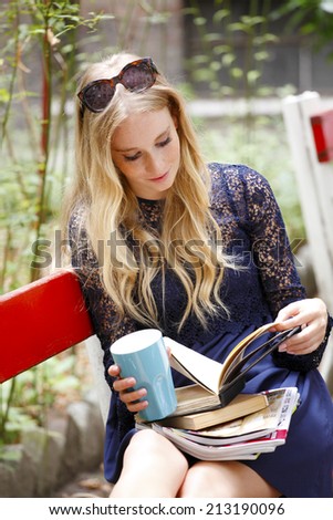 Portrait of attractive female student reading book, while sitting at campus area. Student life.
