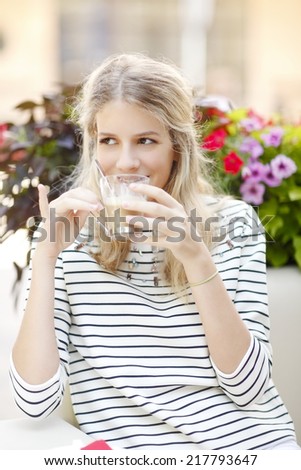 Beautiful young casual woman sitting at bistro outside while drinking cappuccino. City life.