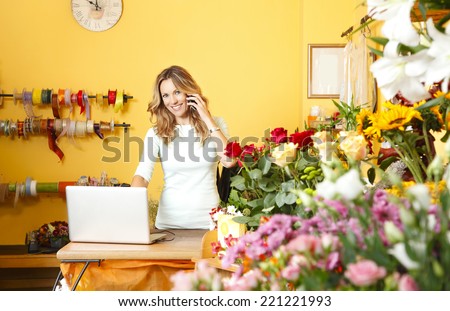 Portrait of mature flower shop owner using her telephone and laptop to take delivery service for her store.