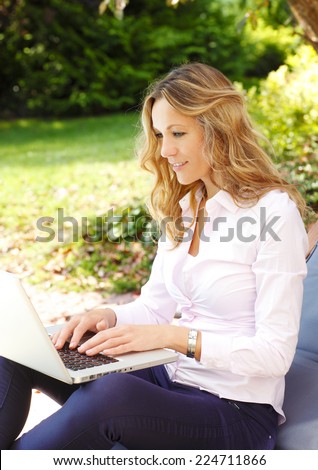 Beautiful mature woman writing her blog on laptop, while sitting at garden.