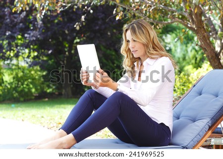 Portrait of middle age mother sitting at garden at home while using personal banking at digital tablet.