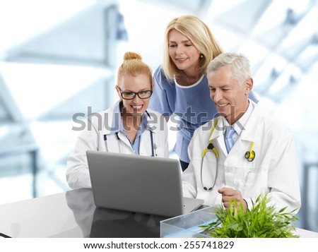 Portrait of three doctors working on laptop., while sitting at desk at private clinic.