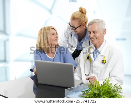 Portrait of three doctors working on laptop., while sitting at desk at private clinic.