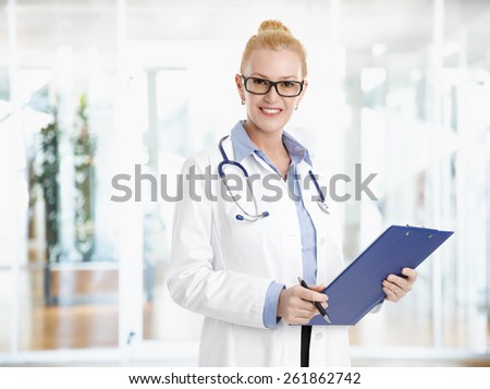 Portrait of female doctor standing at clinic and holding clipboard while checking list of patients.
