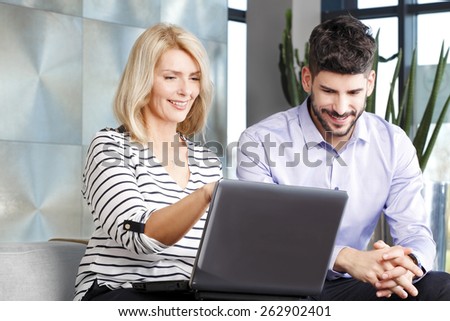 Portrait of middle age business woman sitting at office with young sales man and consulting. Business people analyzing financial data at computer.