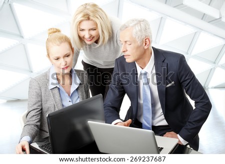 Portrait of businesswoman and businessman sitting in front of computer while sales woman standing in background. Business team working on presentation at office.