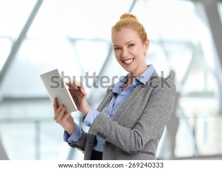 Executive businesswoman standing at office while holding digital tablet in her hands and looking at camera. Business person at work.