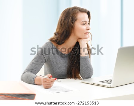 Portrait of young student sitting in front of laptop and thinking. Writing notes to preparing for her financial exam.