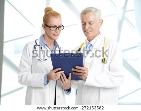 Image of medical team consulting. Portrait of female doctor holding clipboard and consulting with senior doctor while standing at private clinic.