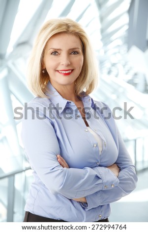 Waist up portrait of beautiful middle age businesswoman standing at office while looking at camera.
