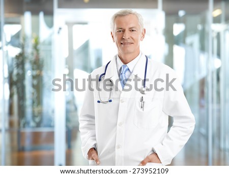 Portrait of healthcare worker. Image of senior male doctor wearing lab coat and standing at private clinic while looking at camera and smiling.