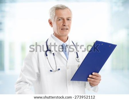 Portrait of senior doctor holding clipboard and checking patient list while standing at hospital.
