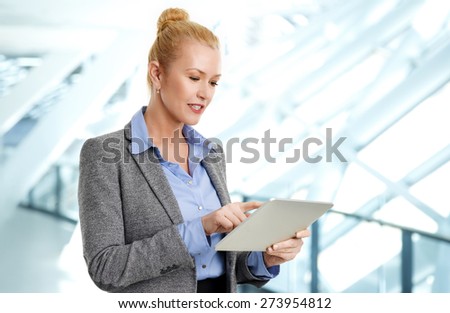 Image of mature businesswoman standing at office and holding digital tablet while surfing on net.