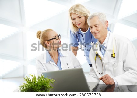 Image of female doctor and male doctor consulting with nurse while sitting at hospital in front of laptop.