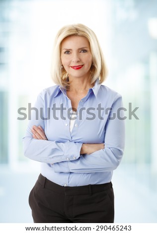 Portrait of middle age businesswoman standing at office with arms crossed. Mature woman looking at camera and smiling.
