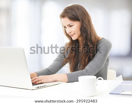 Portrait of sales woman sitting at office in front of laptop and working on her presentation. Young woman typing on keyboard.
