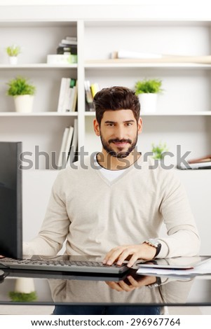 Portrait of handsome bearded graphic designer at workplace. Young creative man sitting in front of computer and checking emails at office. Small business.