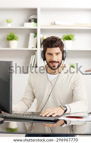 Portrait of handsome bearded graphic designer at workplace. Young creative worker sitting in front of computer and surfing on internet while listening music online at office..