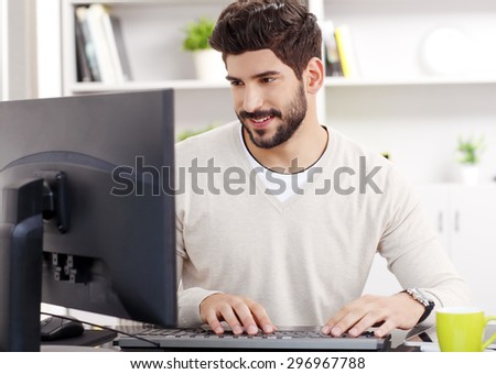 Close-up portrait of handsome bearded graphic designer at workplace. Young creative man sitting in front of computer and checking emails at office. Small business.