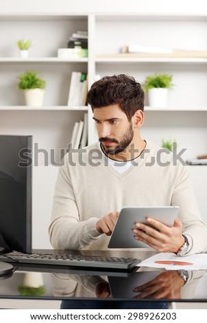 Portrait of young creative sitting at office. Businessman sitting at desk in front of computer and holding hands digital tablet while working on new project.