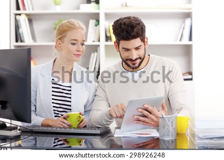 Portrait of business people sitting at office in front of computer. Casual businesswoman and businessman working together. Young professional holding in hand a digital tablet and touching the screen.