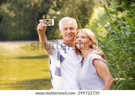 Portrait of happy senior people standing at lakeside while elderly man taking self portrait with his mobile phone.