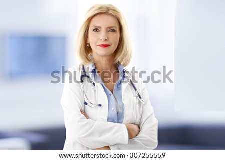 Portrait of middle age female doctor is wearing a white doctor\'s coat with a stethoscope around her neck. Smiling physician standing at private clinic and looking at camera.