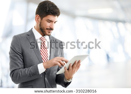 Portrait of young broker standing at office while holding digital tablet in his hands. Young businessman touching digital tablet and checking financial data.