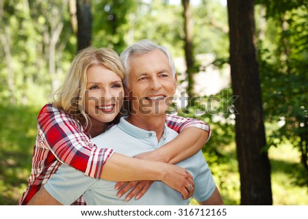 Portrait of active senior couple strolling in the forest while elderly woman arm around her husband.