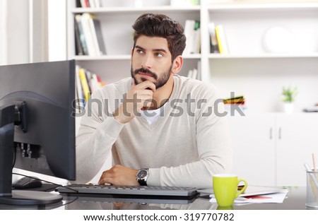 Portrait of young creative sitting at office and working while he thinks the solution of the problem.