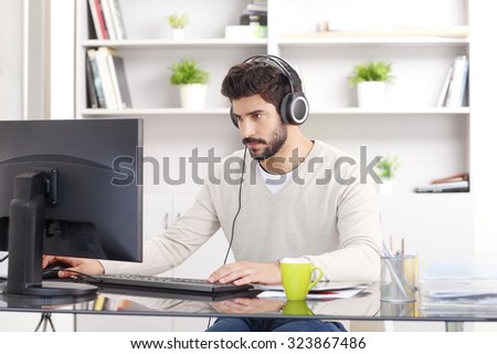 Portrait of young creative with headphone sitting in front of computer at office and listening music online.