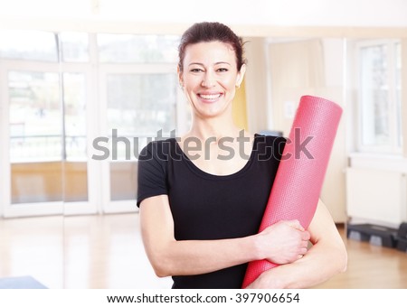 Portrait of a smiling middle age woman holding in her hand a yoga mat after doing yoga.